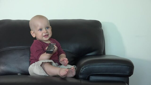 Caucasian boy sit on sofa with remote control. Cheerful child have fun at home