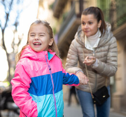 Obraz premium Naughty 5 year old girl in colorful jacket crying and shouting while mother trying to calm her outdoors
