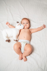 Cute baby in diapers lying on a white sheet with a plush toy. The view from the top. Concept of a happy childhood