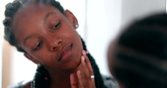 Teen girl removing acne zit in front of mirror. Black African ethnicity