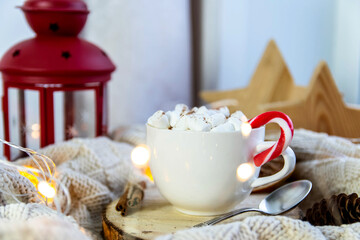 Close-up white cup with coffee and marshmallows, lollipop. Around the plaid, garland. The concept of comfort, hygge.