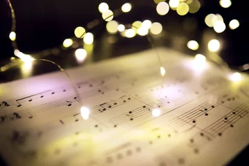  Old sheet with Christmas music notes as background against blurred lights. Christmas music concept © alexkich