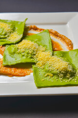 Green ravioli with spinach and meat inside and parmesan cheese on top served in white square plate. Italian cuisine.