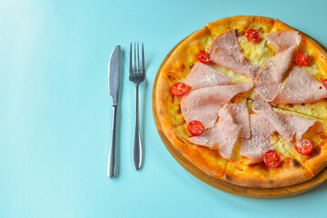 Pizza with bacon, salami and vegetables. Ham and tomatoes pizza with melted cheese. Over pastel blue background.