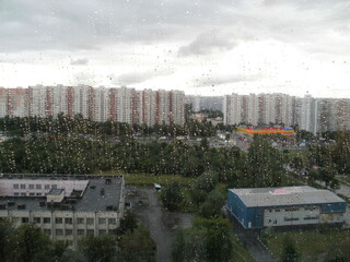 Large drops on the background against the background of city buildings, gray sky and green trees
