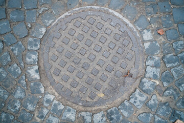 An old sewer hatch on a road made of stones. Old rusty circle sewer hatch. 
