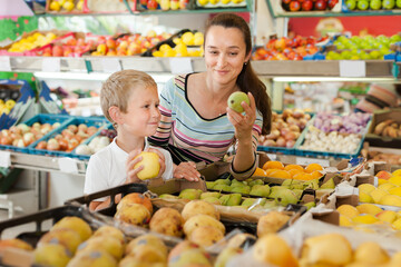 Boy with his brunette mother choosing fresh pears and apples at fruit department of supermarket