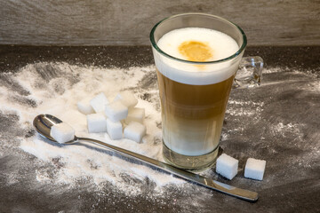 Latte Macchiato im Glas mit langem Löffel und Zuckerwürfeln, angerichtet mit Puderzucker