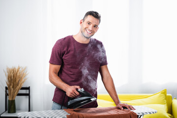  man holding iron with steam near clothes on board at home