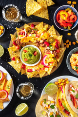 Mexican food, various dishes, overhead shot on a black background. Nachos, tacos, tequila