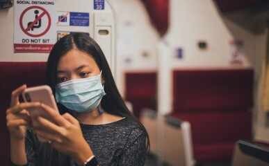 Asian woman wearing face mask and using smartphone sitting on the train.Concept of public transportation Carefully during the outbreak of COVID 19.