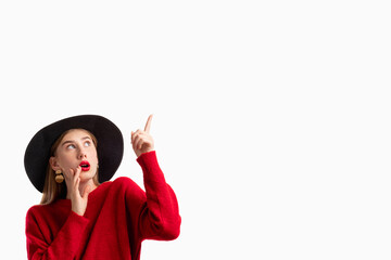Seasonal sale. Shocked offer. New trend style. Information banner. Surprised woman in red sweater black hat pointing looking up isolated on white copy space.