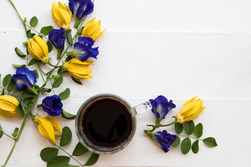 hot black coffee with yellow flower ylang ylang ,blue flower butterfly pea local flora of asia arrangement flat lay style on background white wooden