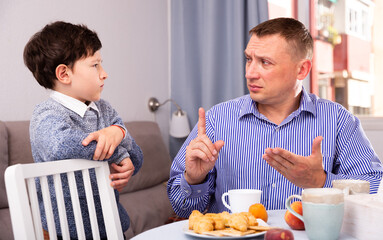 Offended son and unhappy father having quarrel in domestic interior