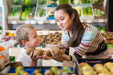 Fototapeta premium Portrait of happy cheerful smiling woman and her little son choosing kiwi at shop