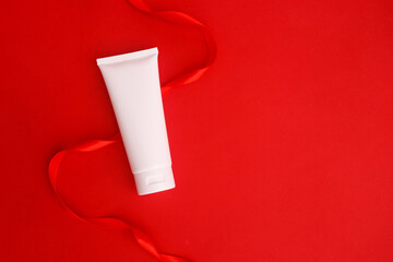 Spa cosmetic product mock up. White cream tube with ribbon on red isolated background. Minimalism concept. Flat lay, copy space, top view