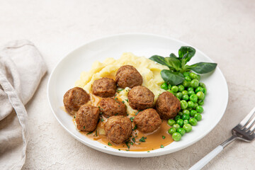 meatballs with mashed potato, cream sauce and green peas on white plate