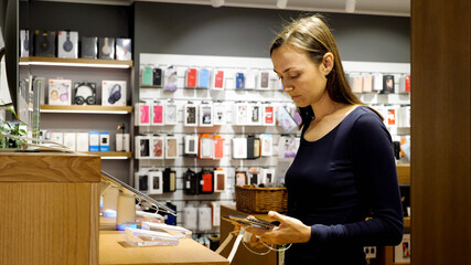 Young woman chooses a new smartphone in an electronics store. Female client is holding two smart phones and comparing it.