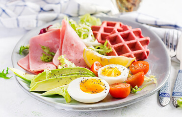 Breakfast with beetroot waffles, boiled egg, ham, tomato and slice avocado on white background. Appetizers, snack, brunch. Healthy food.