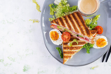 Grilled club sandwich panini with ham, tomato, cheese, avocado and cup of coffee. Delicious breakfast or snack. Top view, flat lay