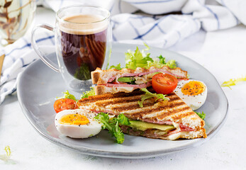 Grilled club sandwich panini with ham, tomato, cheese, avocado and cup of coffee. Delicious breakfast or snack.