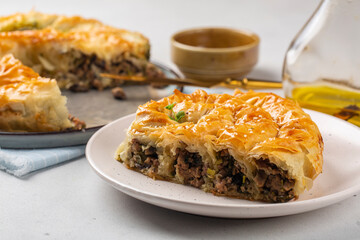 Rolled Burek - savoury pie fith meat and mushrooms feeling, decorated with sesam seedes. Peace of pie on a white table.