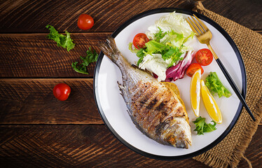 Delicious grilled dorado or sea bream fish with salad, spices, grilled dorada on a wooden table. Top view, flat lay, overhead