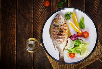 Delicious grilled dorado or sea bream fish with salad, spices, grilled dorada on a wooden table. Top view, flat lay, overhead