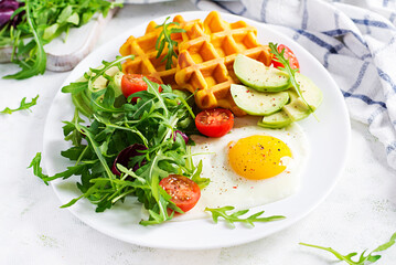Breakfast with pumpkin waffles, fried egg, tomato, avocado and arugula on white background. Appetizers, snack, brunch. Healthy vegetarian food.