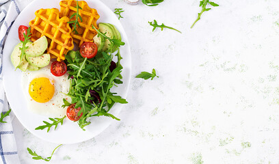 Fototapeta na wymiar Breakfast with pumpkin waffles, fried egg, tomato, avocado and arugula on white background. Appetizers, snack, brunch. Healthy vegetarian food. Top view, overhead, copy space