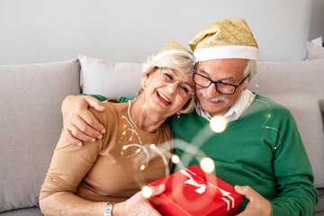 Photo of Happy senior couple exchanging Christmas presents during the day at home. Elderly woman giving present to her beloved husband. Gray hair couple celebrating New Year..