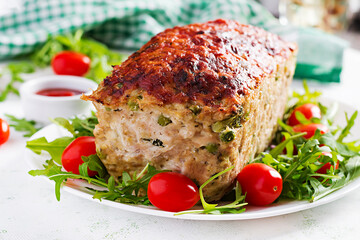 Tasty homemade ground baked chicken meatloaf with green peas and sliced broccoli on white table. Food american meat loaf