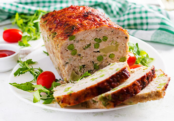 Tasty homemade ground baked chicken meatloaf with green peas and sliced broccoli on white table. Food american meat loaf
