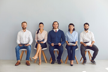 Smiling candidates job seekers sitting in row with resumes in hand and waiting for interview invitation turn