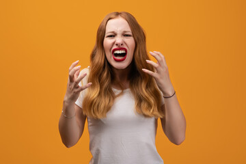 Angry young woman with wavy redhead, screaming on yellow studio background