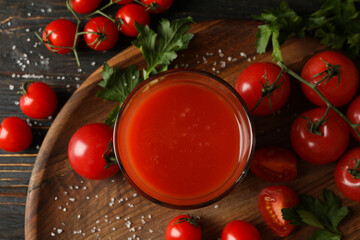 Glass of tomato juice, tomatoes and salt on wooden background