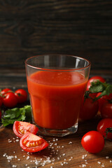 Glass of tomato juice, tomatoes and salt on wooden background