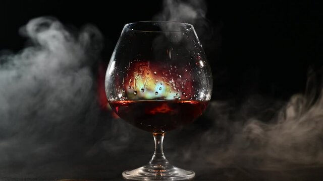 A glass of brandy and cigar smoke in the dark on the background of the fireplace. Gentlemen's club concept