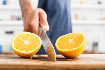 Close up of halves of juicy orange and wet knife in hand of man on blurred background
