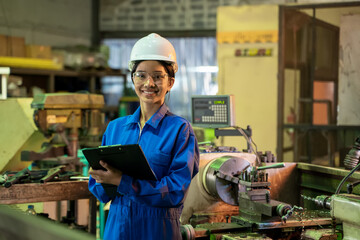 Female industrial worker in protective uniform working and checking machine in a large industrial...