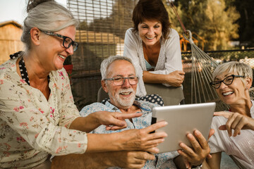 Group of senior friends with eyeglasses using digital tablet, having fun.
