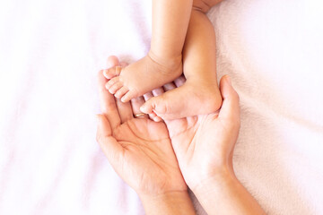 Obraz na płótnie Canvas Mother hands holding baby feet lying on a comfortable bed at home,Family concept