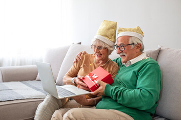 Senior couple in santa hat waving while having a video call on laptop at home. social distancing during covid-19 coronavirus quarantine lockdown. Christmas holidays in quarantine