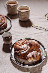 Cinnamon swirl brioche or Cinnamon roll bun and cups of cocoa on greige linen tablecloth. Homemade baked swedish cinnamon roll. Kanelbullar. Cozy winter breakfast