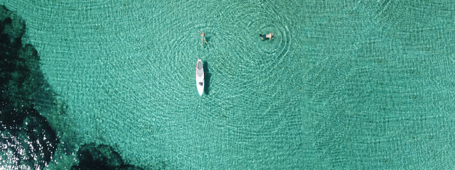 Aerial drone ultra wide top down photo of fit unidentified woman paddling on a SUP board or Stand...