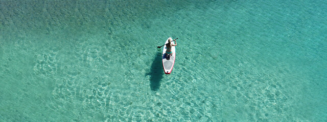 Aerial drone ultra wide top down photo of fit unidentified woman paddling on a SUP board or Stand...