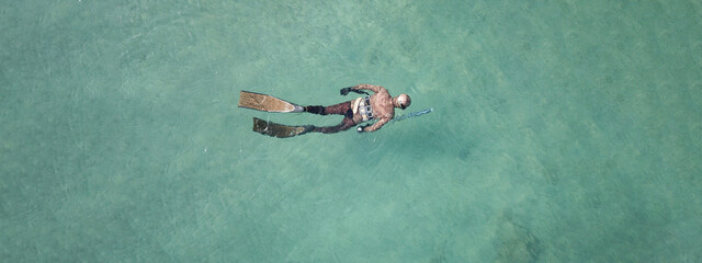 Aerial drone top down ultra wide panoramic photo of spearfishing scuba diver in tropical exotic shallow bay with turquoise clear waters