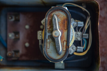 On rough wall, floor, paint peels off. Corrosion and rust of metal. Electrical board. Old, broken distribution point Electrical cables sticking out of an electrical panel from an old rusty iron box