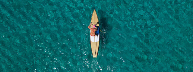 Aerial drone ultra wide top down photo of fit unidentified woman paddling on a SUP board or Stand...