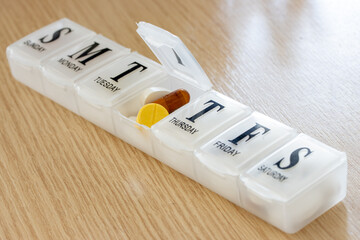 A medicaments in a plastic box with descriptions of each day of use. A open pillbox with tablets...